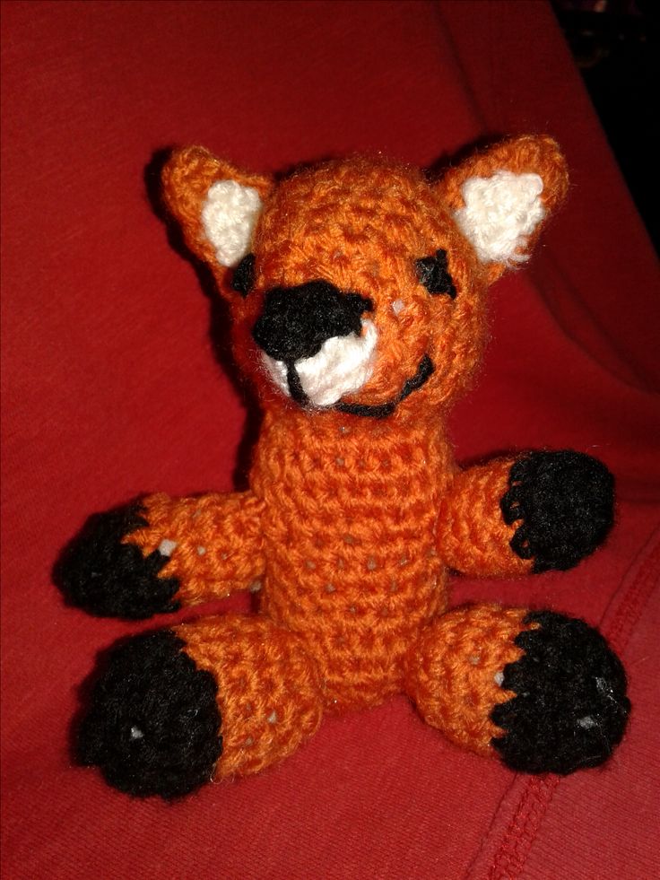 a crocheted orange stuffed animal sitting on top of a red blanket with black feet