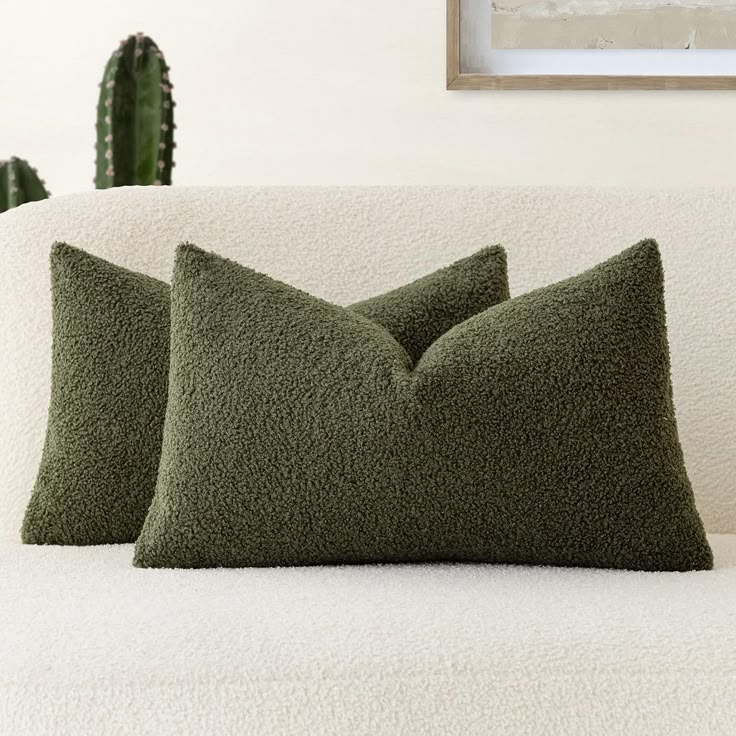 two green pillows sitting on top of a white couch next to a cacti