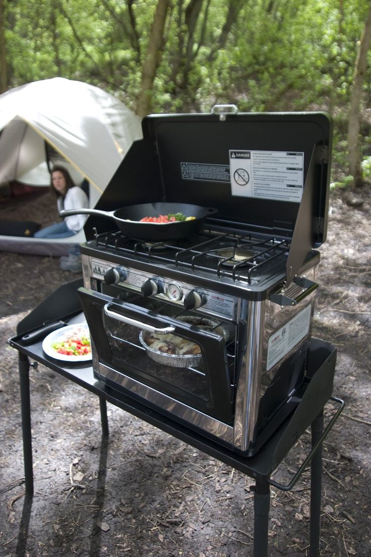 an outdoor stove and grill set up in the woods with a person sitting under it