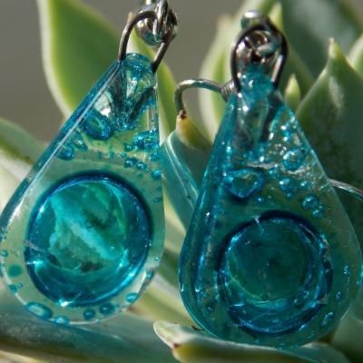 two blue glass earrings sitting on top of a plant