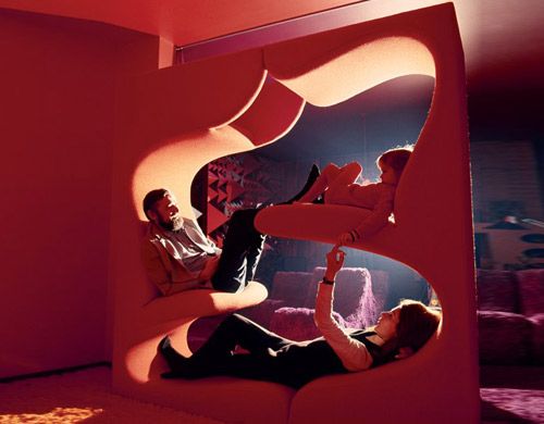 two people sitting on a couch in a room with red walls and floor to ceiling windows