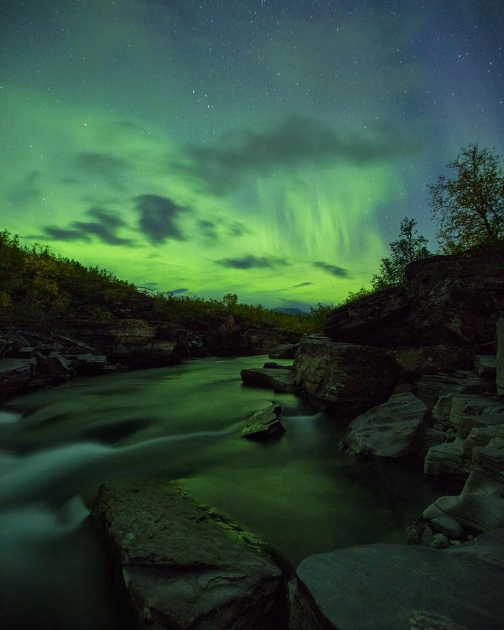 the aurora bore is seen in the sky above some rocks and trees, as well as water