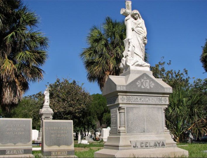 the statue is surrounded by palm trees and headstones in front of a cemetery