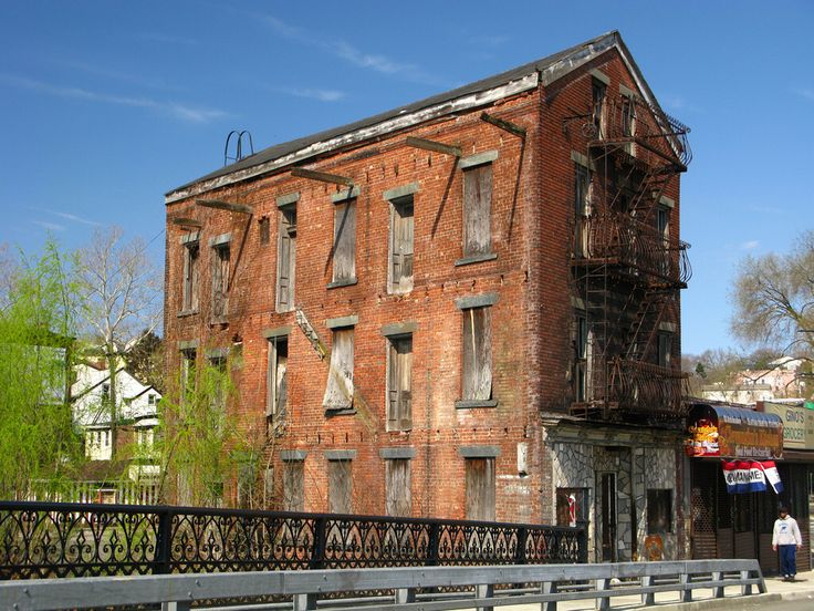 an old red brick building sitting on the side of a road next to a fence