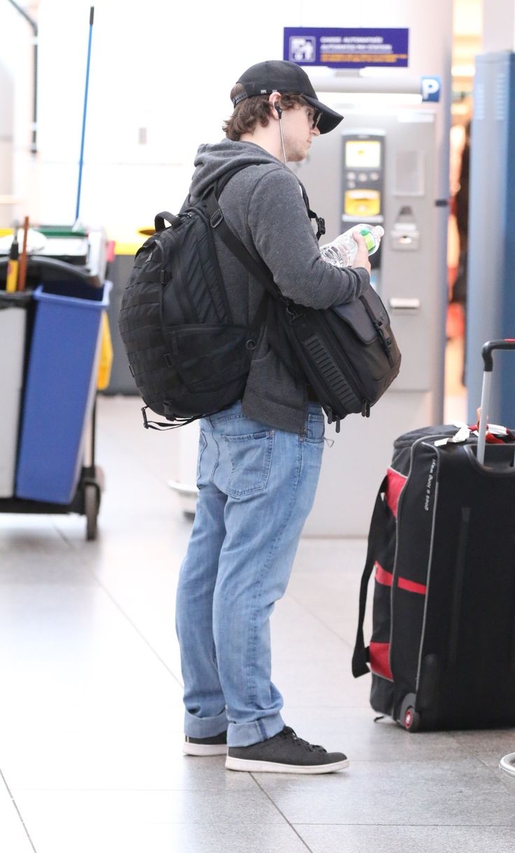 a man standing in an airport with his back to the camera looking at his cell phone