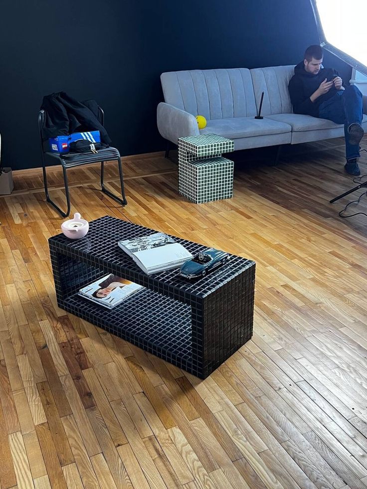 a man sitting on a couch next to a coffee table in a room with hard wood floors