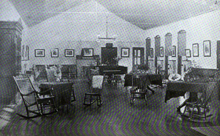 an old black and white photo of a room with many chairs, tables and pictures on the walls