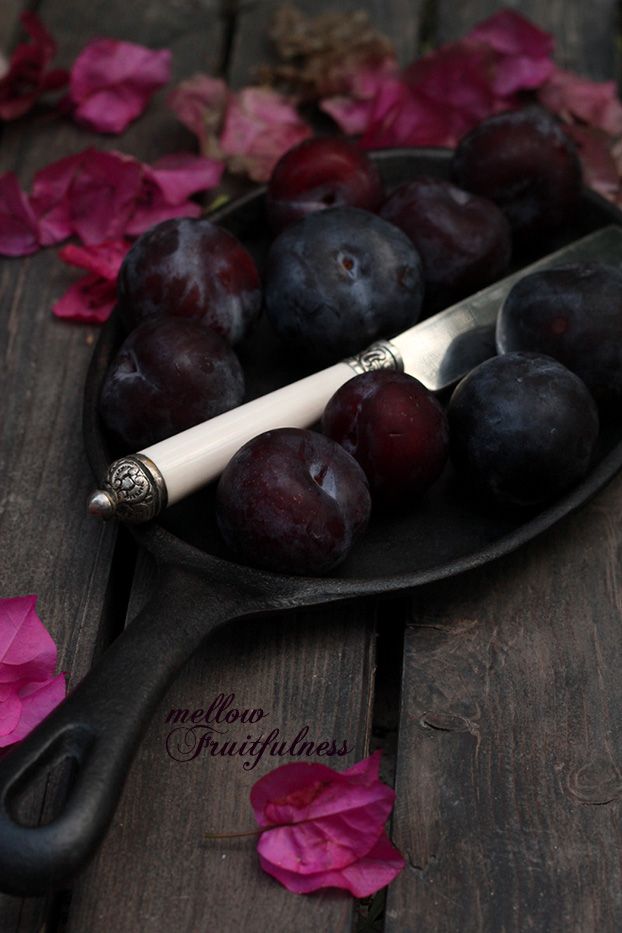 grapes and plums in a bowl with a knife on a wooden table surrounded by pink flowers