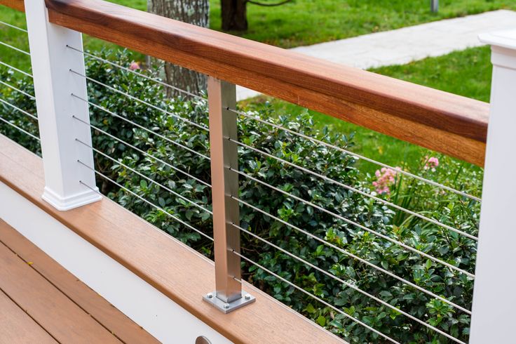 a close up of a wooden and metal railing on a deck with bushes in the background