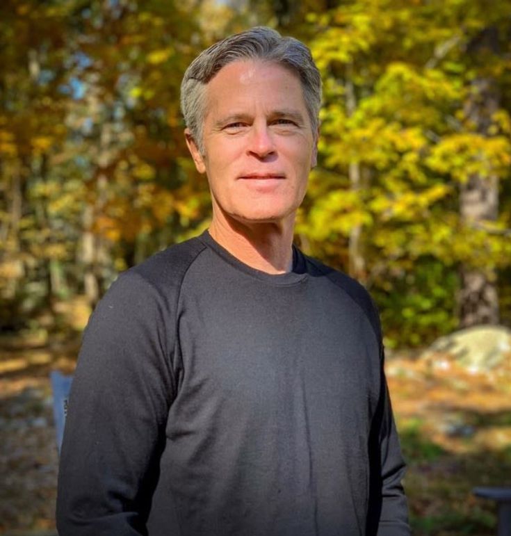 a man standing in front of some trees with his hands on his hips and looking at the camera