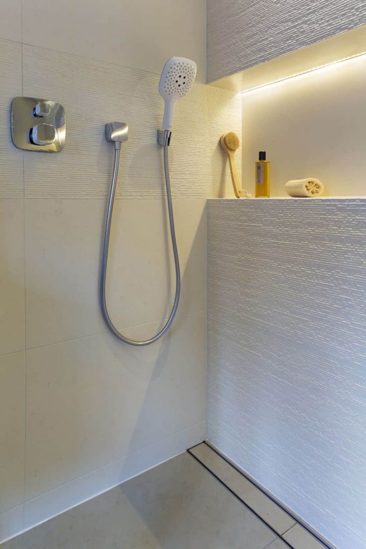 a shower head and hand held shower faucet in a white tiled bathroom with built - in lighting