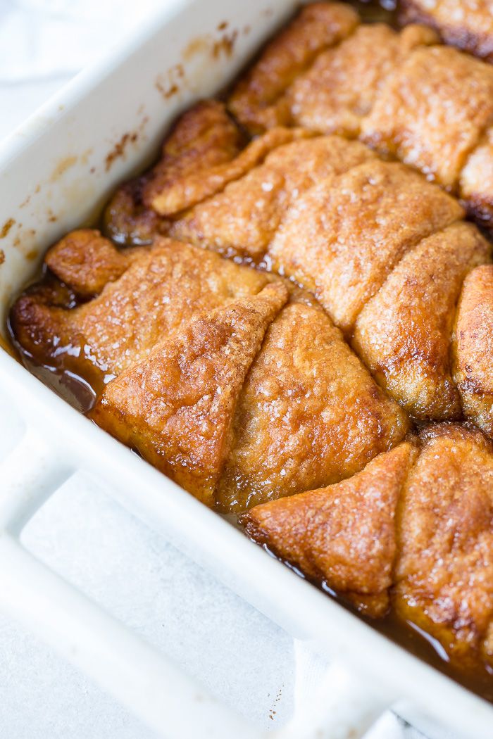 a white casserole dish filled with cinnamon rolls covered in syrup and brown sauce