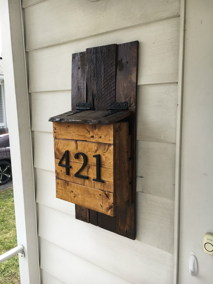 a wooden mailbox mounted to the side of a white house with numbers on it