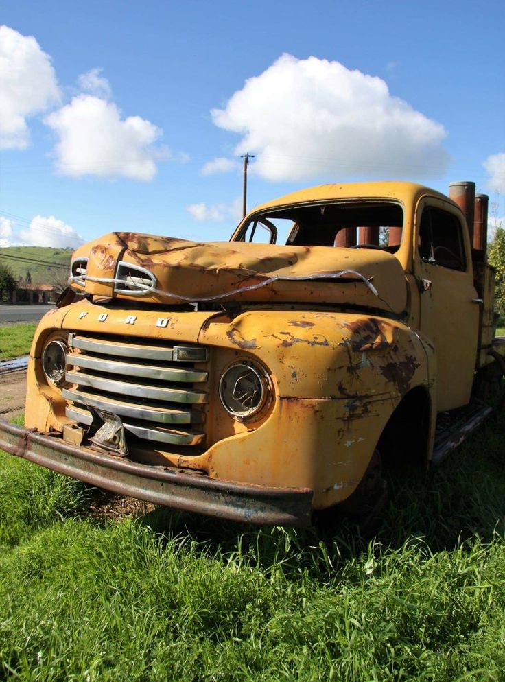 an old yellow truck sitting in the grass