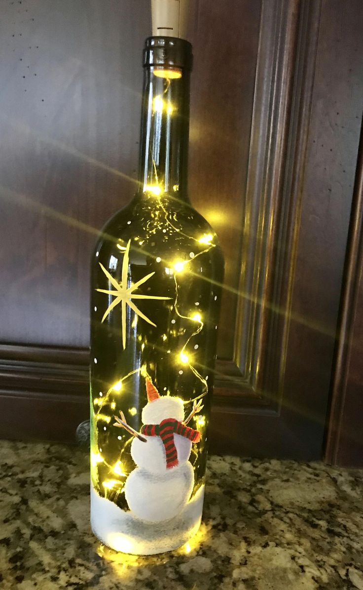 a lighted bottle with a snowman in it on a counter top next to a wall