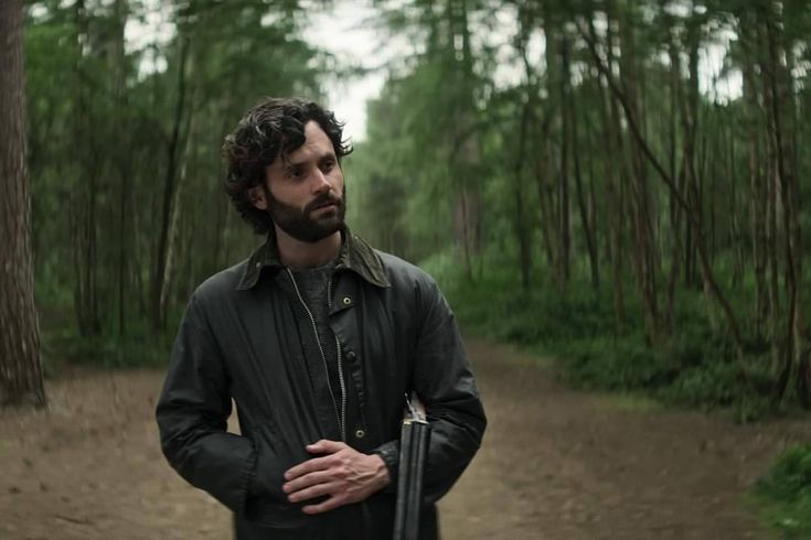 a man standing in the middle of a forest with his hands on his hips and looking off into the distance