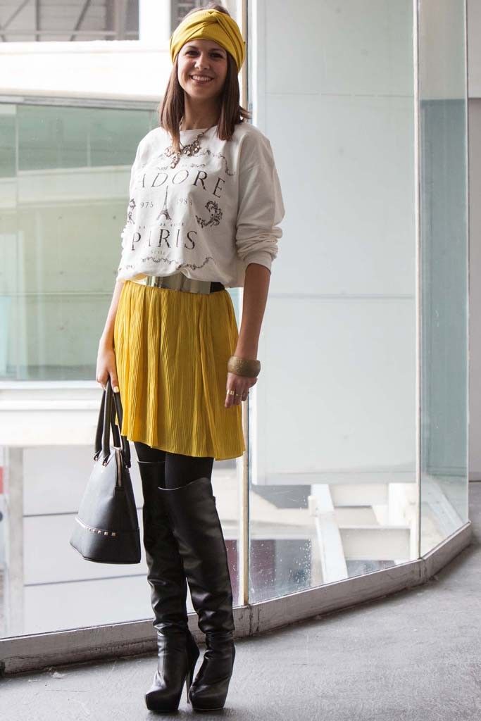 a woman standing in front of a glass wall wearing a yellow skirt and knee high boots