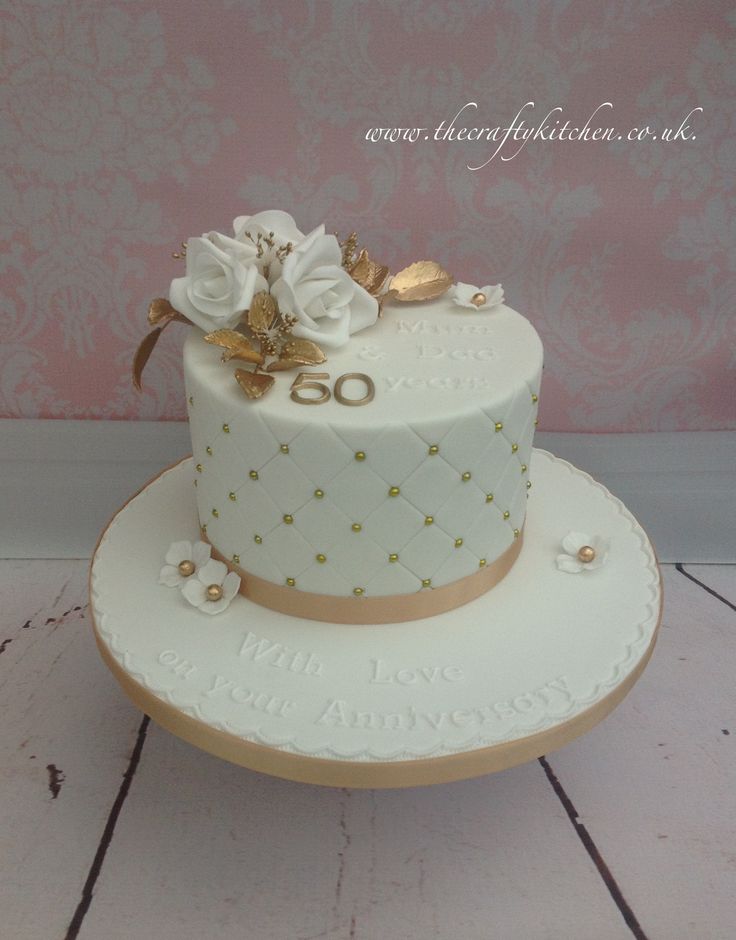 a white and gold wedding cake with flowers on the top is sitting on a wooden table