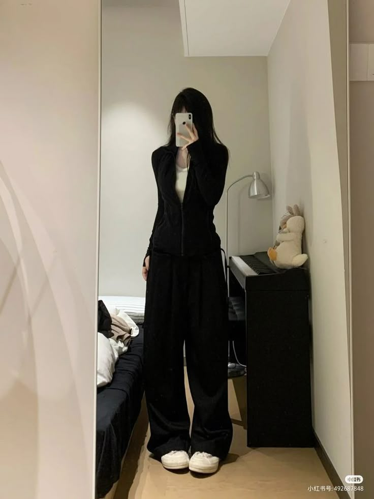 a woman taking a selfie in the mirror while wearing black clothing and white shoes