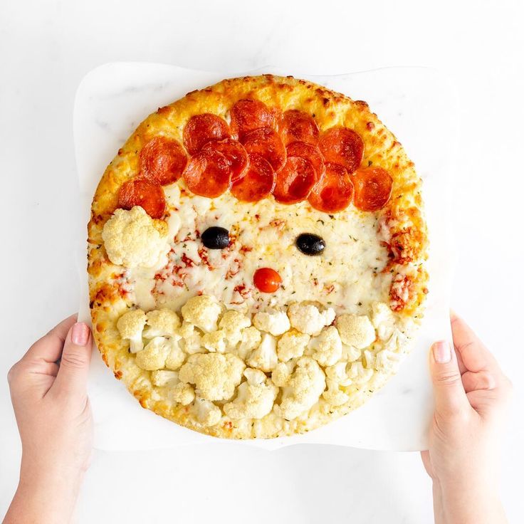 a pizza that has been made to look like a face is being held by two hands