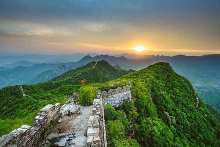 the great wall of china is surrounded by mountains and greenery as the sun sets