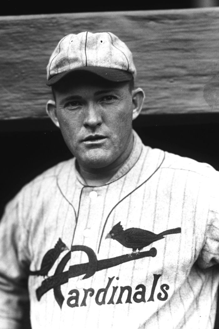 a black and white photo of a baseball player with a bird on his shirt, standing in the dugout