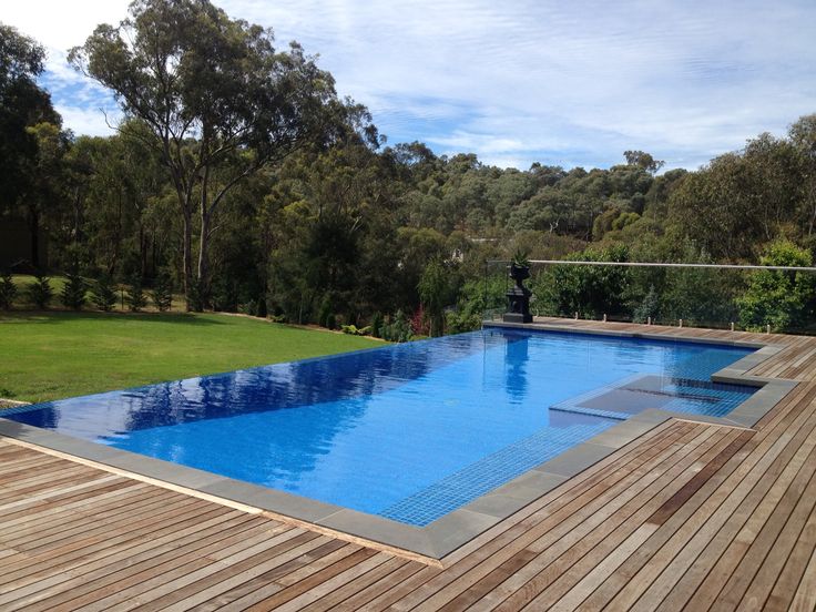 an empty swimming pool in the middle of a wooden decked area with grass and trees