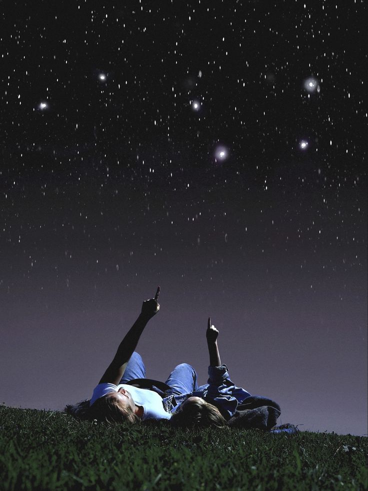 two people laying in the grass under a night sky with stars and planets above them