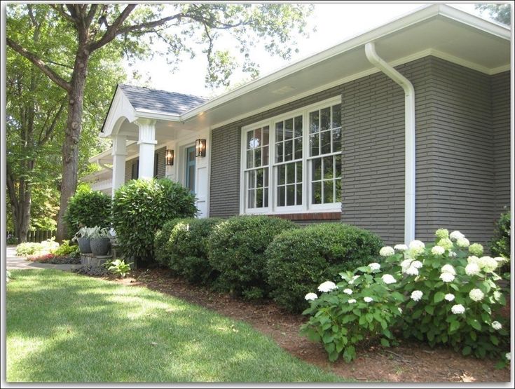 a gray house with white trim and flowers in the front yard on a sunny day