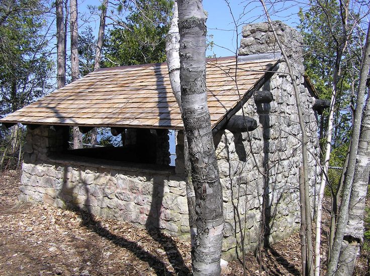 an old stone building in the woods with a roof made out of rocks and logs