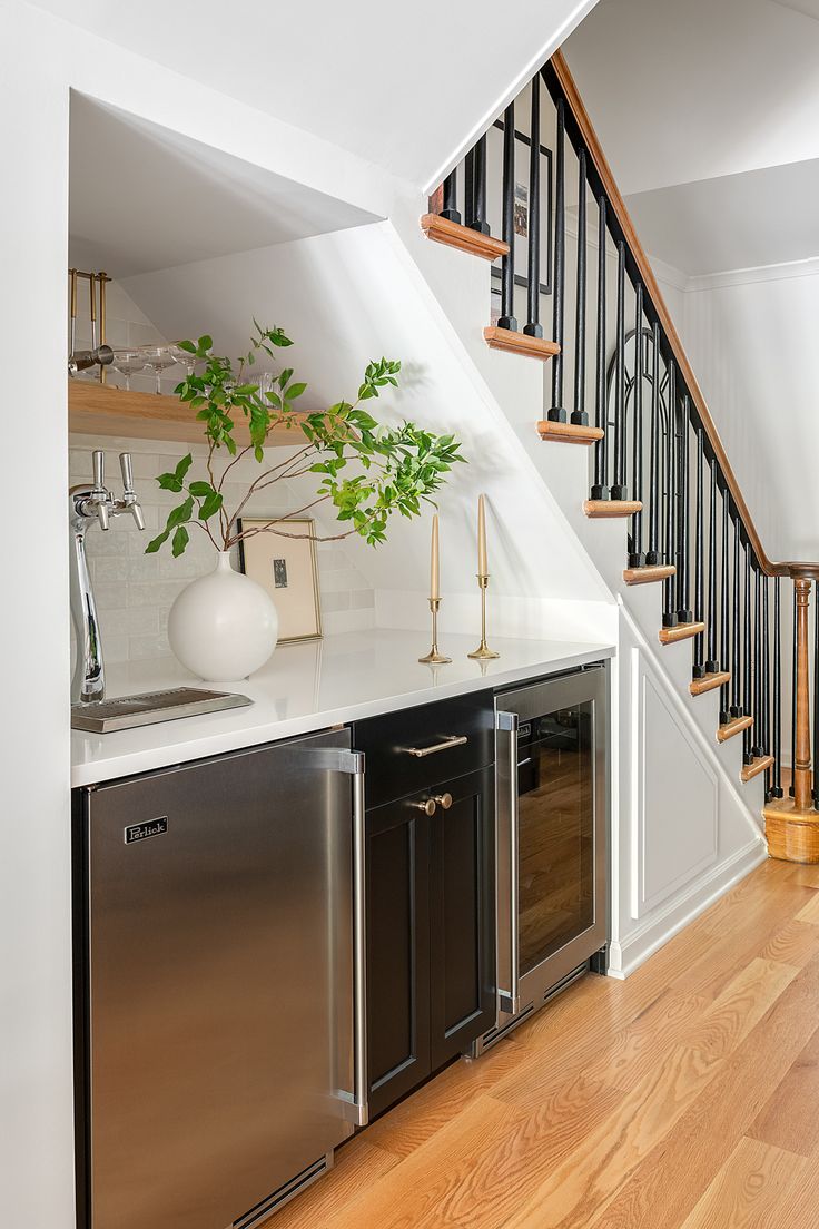 a kitchen with stainless steel appliances and white counter tops next to a stair case that leads up to the second floor