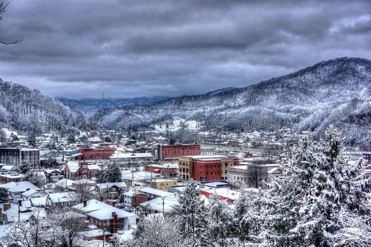 a snowy mountain town surrounded by trees and mountains in the distance with dark clouds overhead