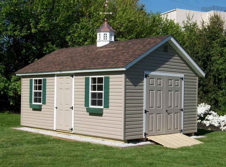 a small gray shed with green shutters and a steeple on the top floor