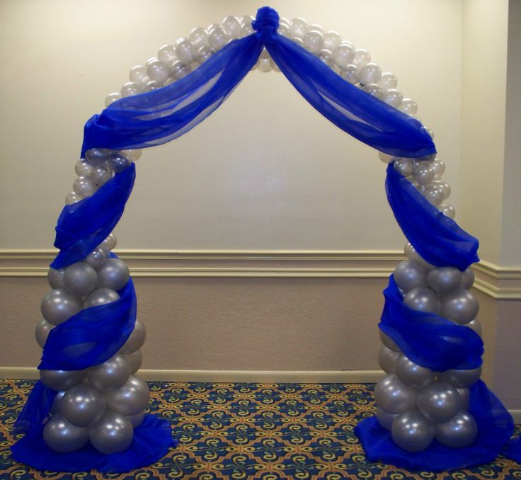 an arch made out of balloons with blue ribbon and white pearls on it in the middle of a room