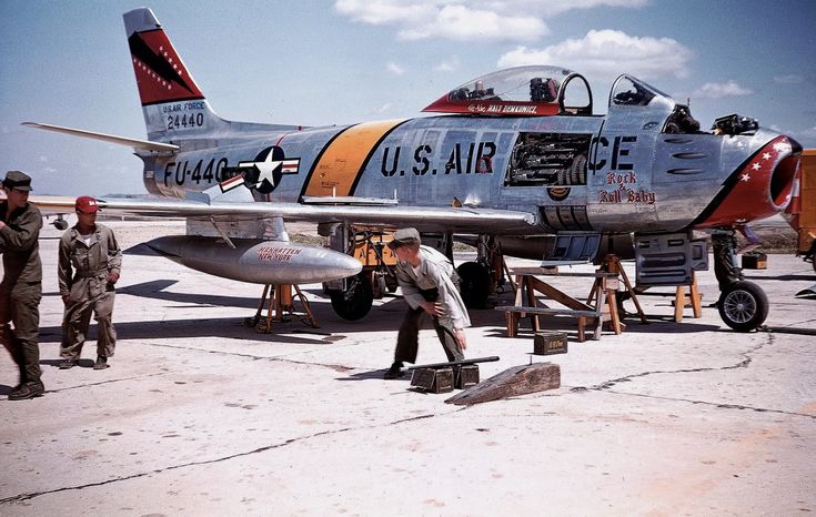 two men working on an airplane in the middle of a runway with other people standing around it