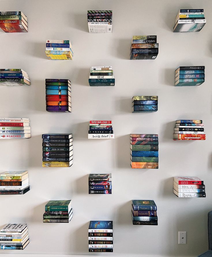 several books are arranged on the wall above a blue chair in front of a white wall