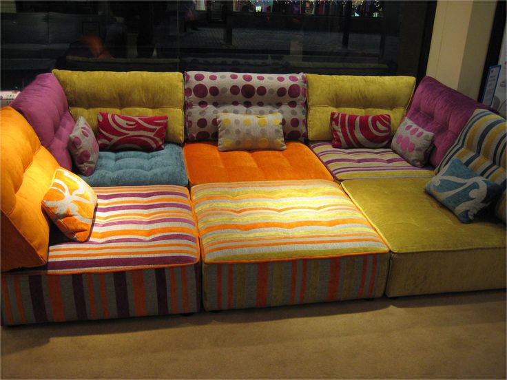 a multicolored couch with pillows on it in front of a window