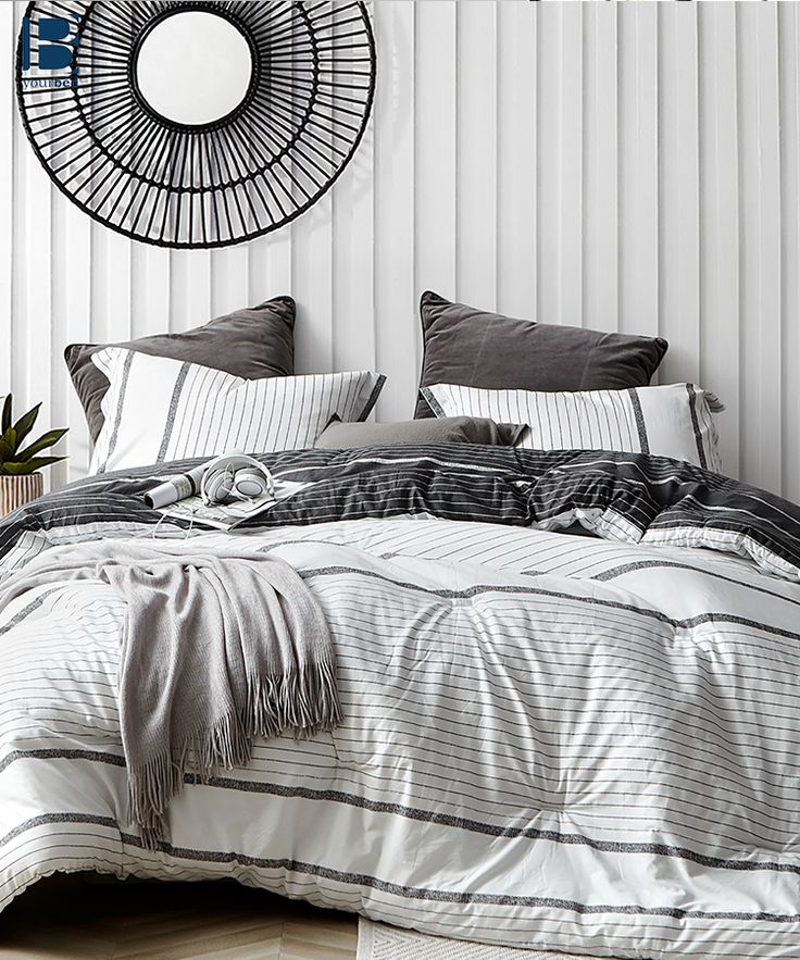 a bed with grey and white striped comforter next to a round mirror on the wall