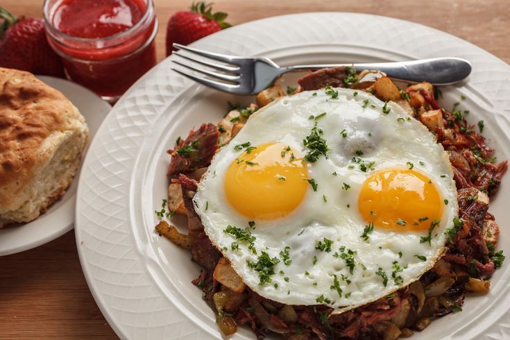 two fried eggs on top of hash browns with strawberry jam in the backgroud