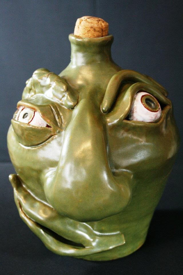 a green ceramic vase with two faces on it's face and a cork top