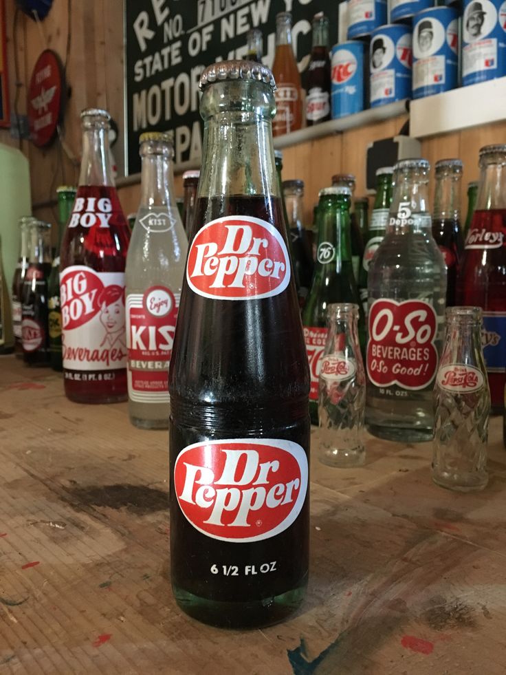 several bottles of dr pepper sit on a wooden table in front of many empty glasses