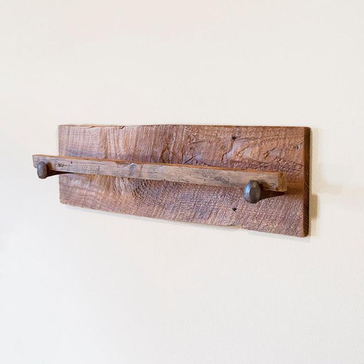 a wooden shelf mounted to the side of a wall with two metal hooks on it