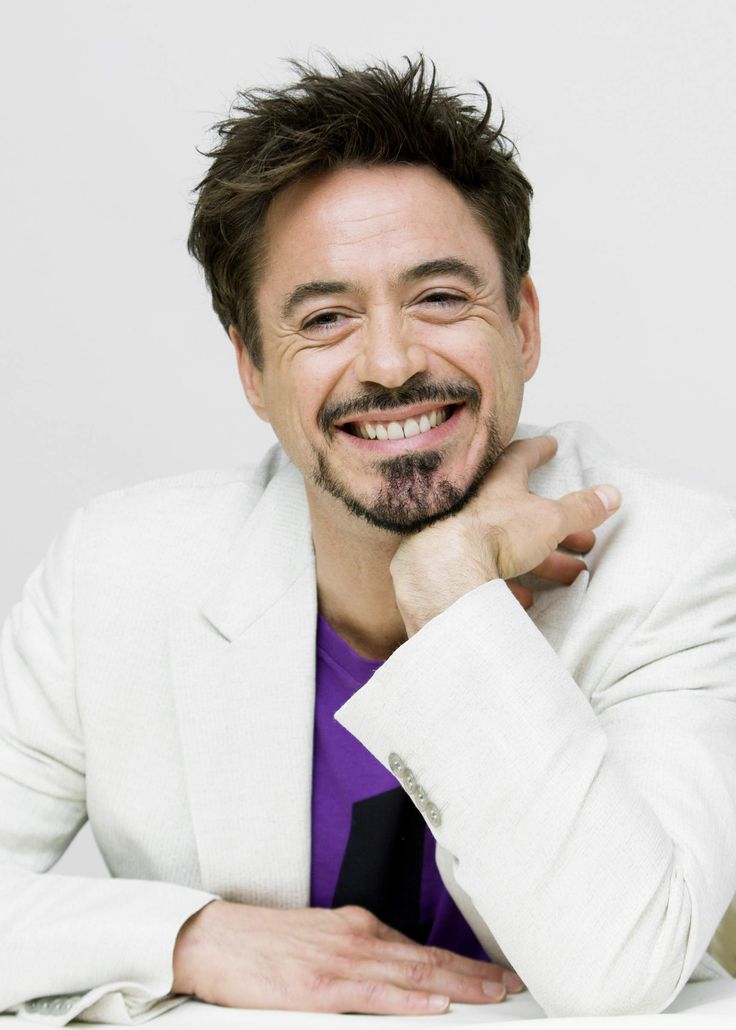 a man with a goatee smiles at the camera while wearing a white jacket and purple shirt