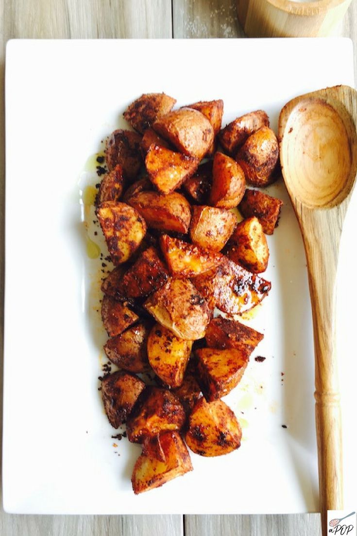 a white plate topped with cooked potatoes next to a wooden spoon on top of a table