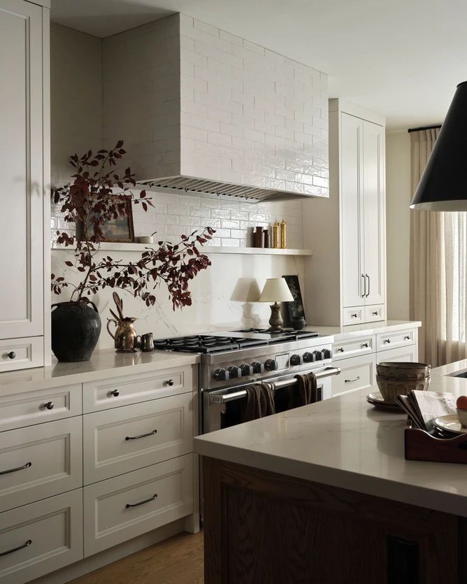 a kitchen with white cabinets and an island in front of a stove top oven that has a potted plant on it