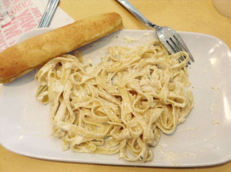 a white plate topped with pasta next to a piece of bread on top of a table