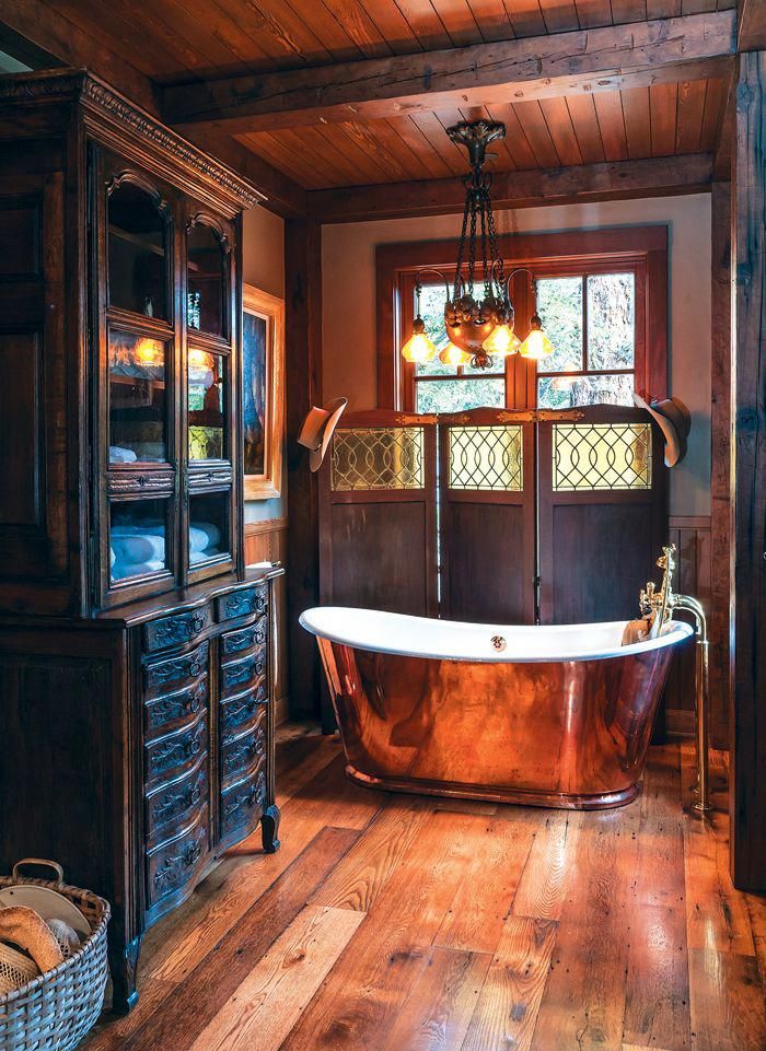 an old fashioned bathtub is in the middle of a wood floored bathroom with wooden cabinets