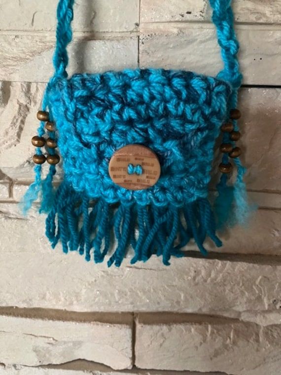 a crocheted purse hanging on a brick wall with a wooden button in the center