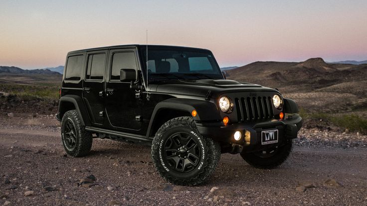 a black jeep parked in the middle of a desert road at dusk with mountains in the background