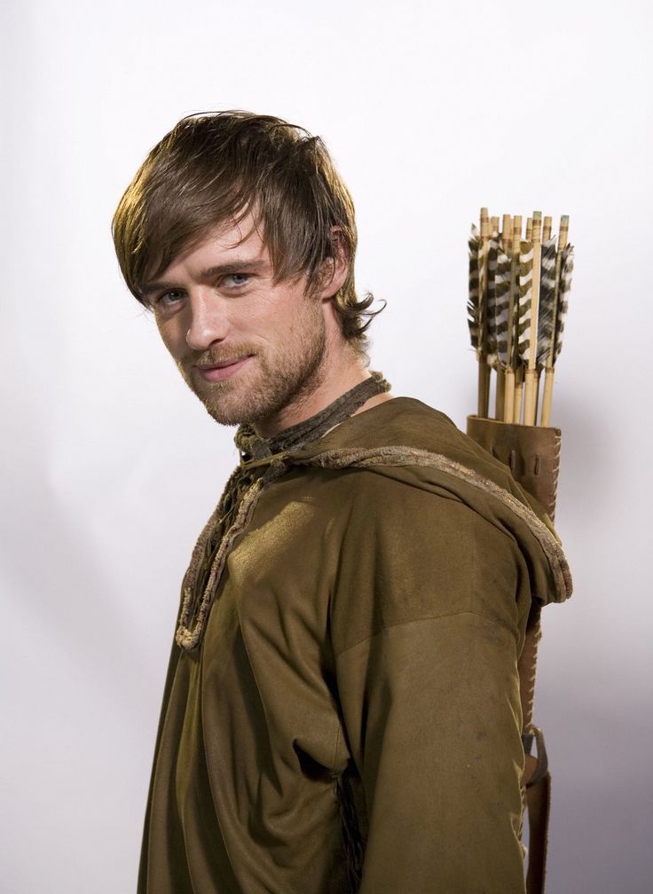 a young man holding two wooden arrows in his right hand and looking at the camera